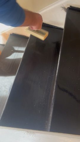 A person is brushing finish on a dark wood stair tread.