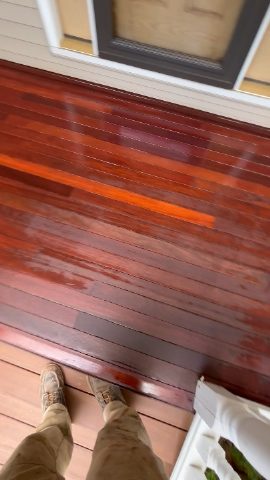 Finished reddish-brown wood floor on an exterior deck or porch by a sliding door.